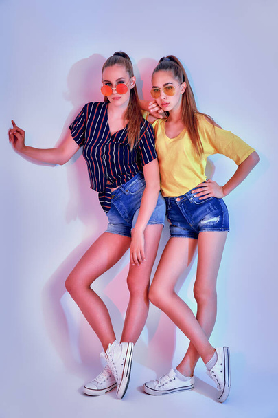 Twee vrouwelijke tieners in zonnebril en zomer kleding poseren in de studio op witte achtergrond - Foto, afbeelding