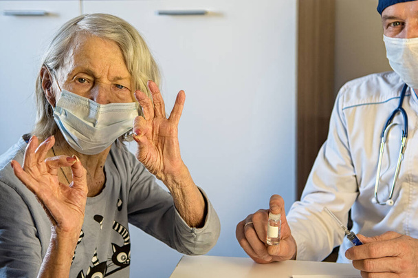 Médecin soignant et grand-mère âgée positive masquée à la maison ou à l'hôpital montrent OK. Concept de vaccination des personnes âgées - Photo, image