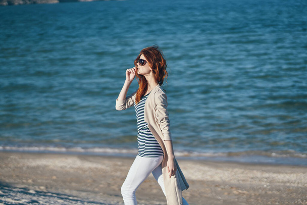 Frau in Sonnenbrille und Hose am Strand in der Nähe des Meeres in den Bergen - Foto, Bild