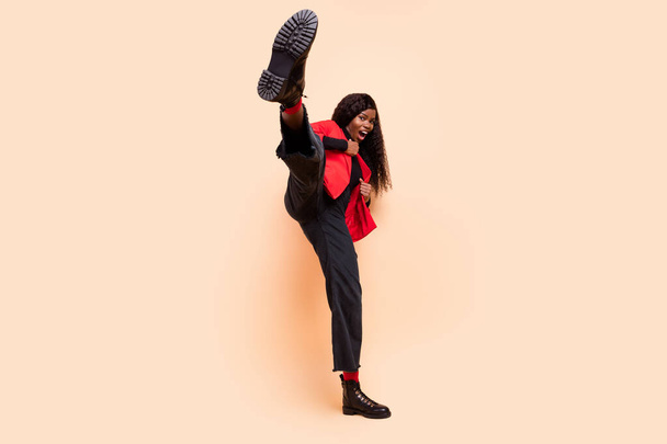 Full length photo of active sportive dark skin woman kick leg karate isolated on pastel beige color background - 写真・画像