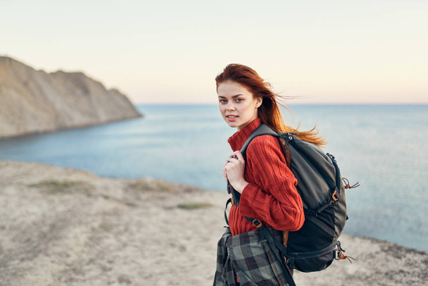 Dağlarda sırt çantalı güzel bir kadın kırmızı süveter model saç stili okyanus denizi - Fotoğraf, Görsel