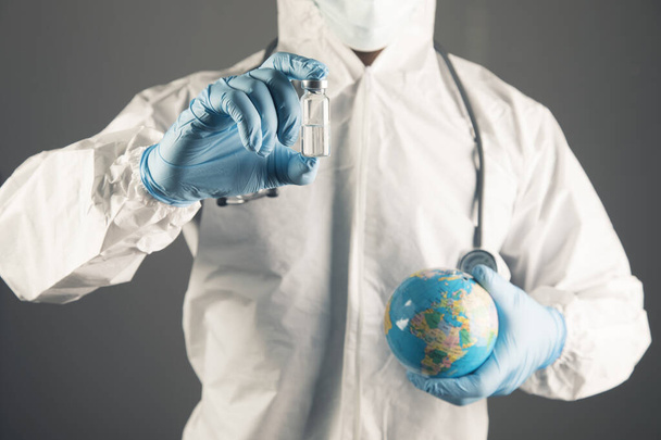 a doctor in protective uniform holds a vaccine and a globe - Zdjęcie, obraz