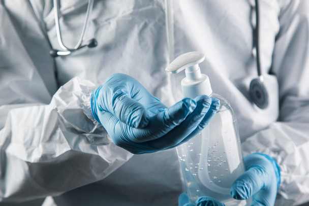 un médecin en uniforme de protection blanc se lave les mains avec un antiseptique sur fond gris - Photo, image