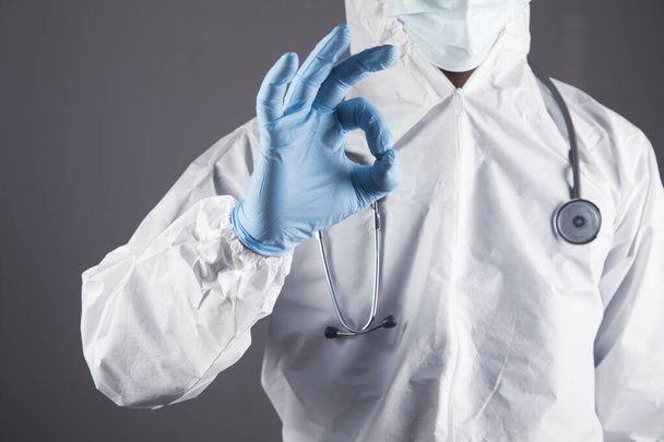 doctor in white protective uniform shows ok on a gray background - Photo, Image