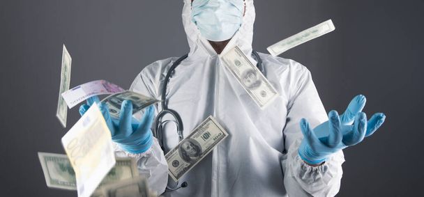 money pours on a doctor in a white coat and gloves on a gray background - Foto, Bild