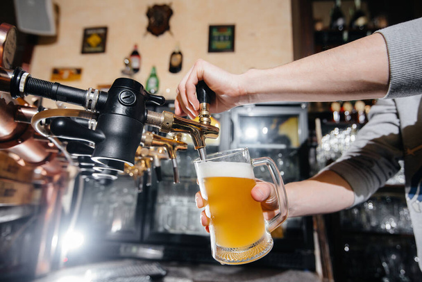 Close-up of the bartender filling a mug of light beer. The bar counter in the pub. - Foto, imagen