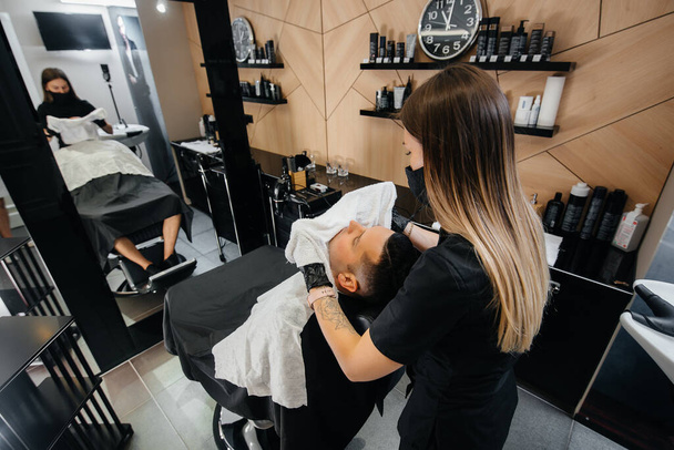 A professional stylist in a modern stylish barbershop shaves and cuts a young man's hair. Beauty salon, hair salon - Fotografie, Obrázek