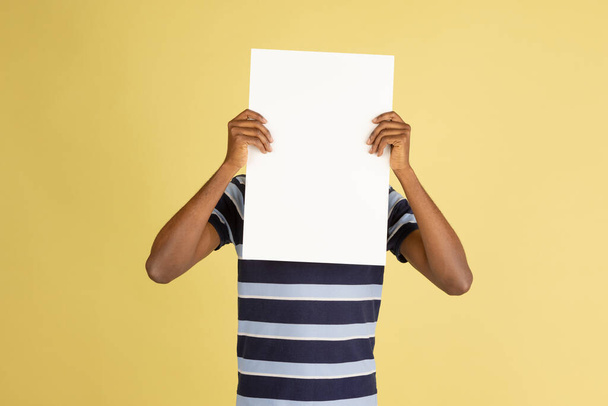 Happy African man with blank sheet of paper isolated over yellow studio background - Fotó, kép