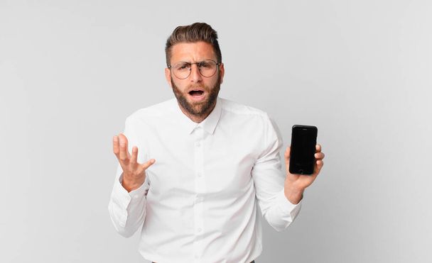 young handsome man looking desperate, frustrated and stressed and holding a cell - Foto, Bild