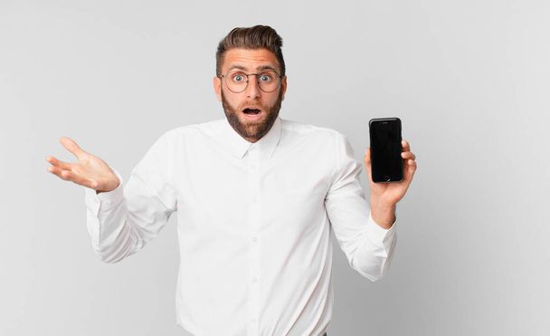 young handsome man feeling extremely shocked and surprised and holding a cell - Foto, imagen