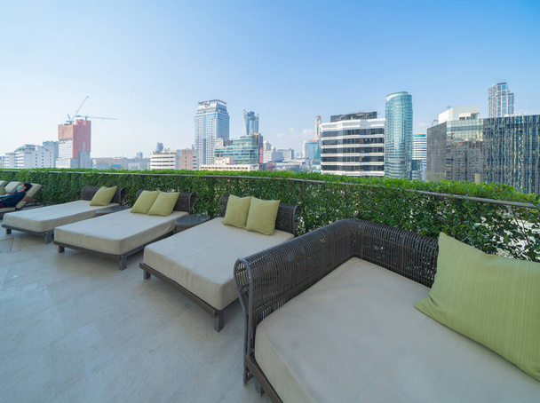 Zon ligstoel, stoel bank onder bedekt op het dak van het hotel gebouw in Bangkok centrum skyline, stedelijk uitzicht op de stad. Ontspannen in het zomerseizoen in reisvakantie concept. - Foto, afbeelding