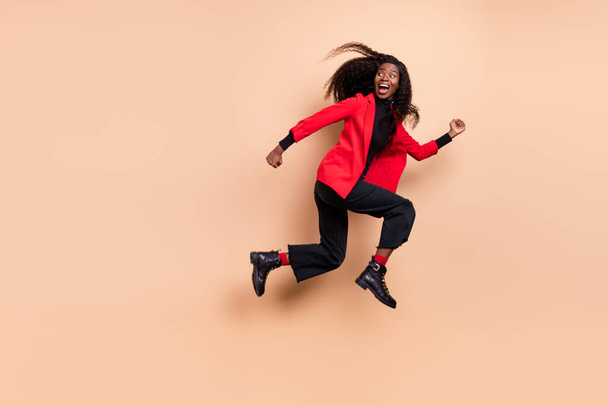 Photo of sweet cute curly dark skin woman dressed red blazer jumping running looking back empty space isolated beige color background - Foto, Imagen
