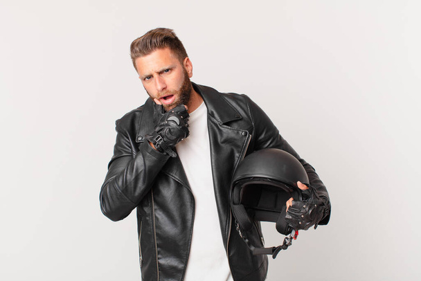 young handsome man with mouth and eyes wide open and hand on chin. motorbike helmet concept - Foto, immagini
