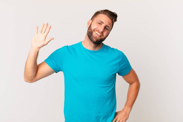 young handsome man smiling happily, waving hand, welcoming and greeting you. fitness concept - Фото, изображение