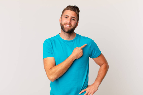 young handsome man smiling cheerfully, feeling happy and pointing to the side. fitness concept - Foto, afbeelding