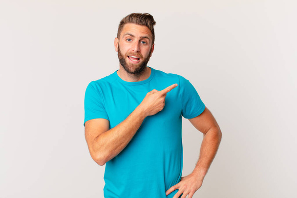 young handsome man looking excited and surprised pointing to the side. fitness concept - Foto, imagen