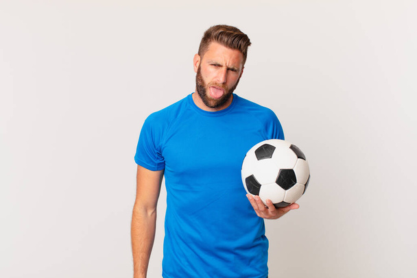 young handsome man feeling disgusted and irritated and tongue out. soccer concept - Photo, Image