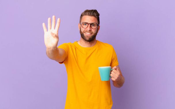young handsome man smiling and looking friendly, showing number four. and holding a coffee mug - Foto, Imagen