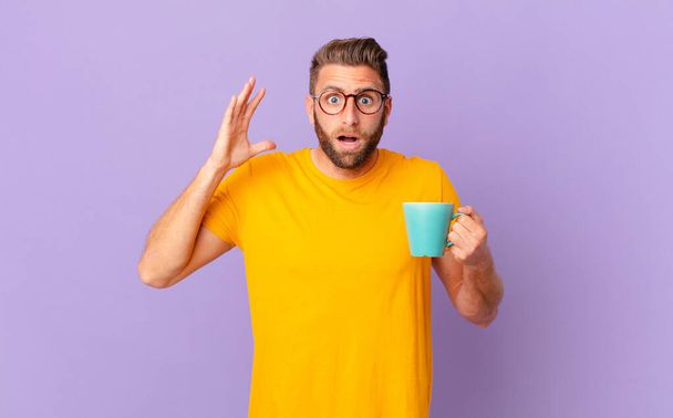 young handsome man screaming with hands up in the air. and holding a coffee mug - Foto, imagen