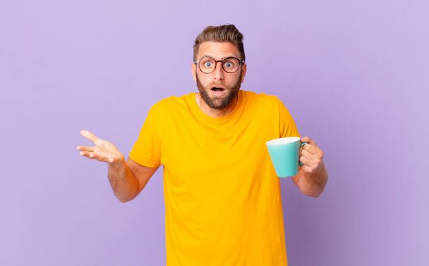 young handsome man feeling extremely shocked and surprised. and holding a coffee mug - 写真・画像