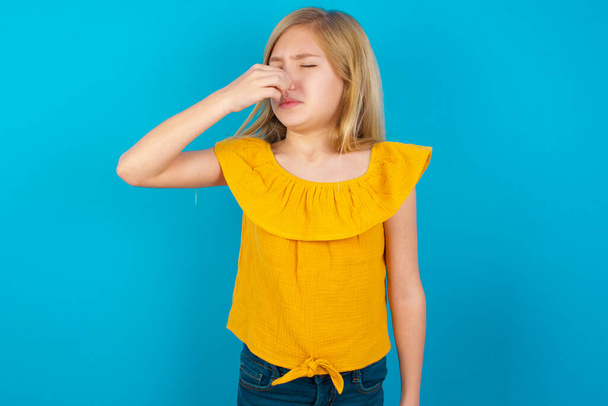 klein meisje ruikt iets stinkends en walgelijk, ondraaglijke geur, houdt adem in met vingers op de neus. Slechte geur - Foto, afbeelding
