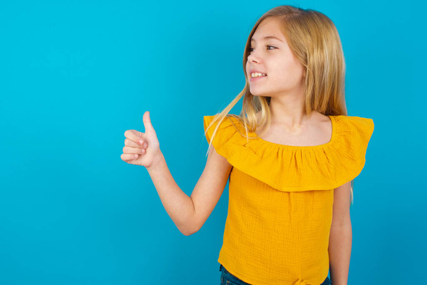little girl Looking proud, smiling doing thumbs up gesture to the side. Good job! - 写真・画像