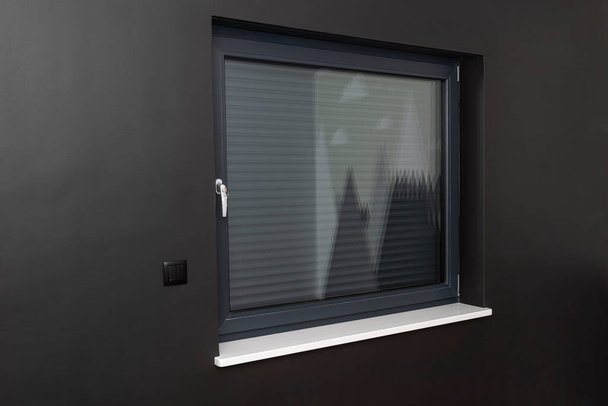 Ein großes Fenster in einem Raum mit schwarzen Wänden, komplett mit Außenjalousien abgedeckt. - Foto, Bild