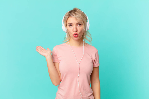 young pretty woman looking surprised and shocked, with jaw dropped holding an object. listening music concept - Foto, Imagen