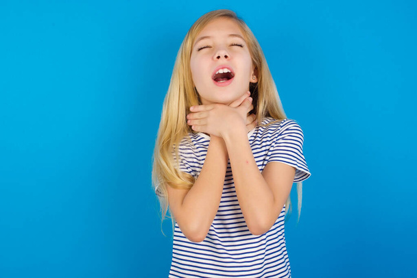 Chica caucásica vistiendo camisa a rayas contra la pared azul, gritando sofocado porque estrangulamiento doloroso. Problema de salud. Concepto de asfixia y suicidio. - Foto, imagen