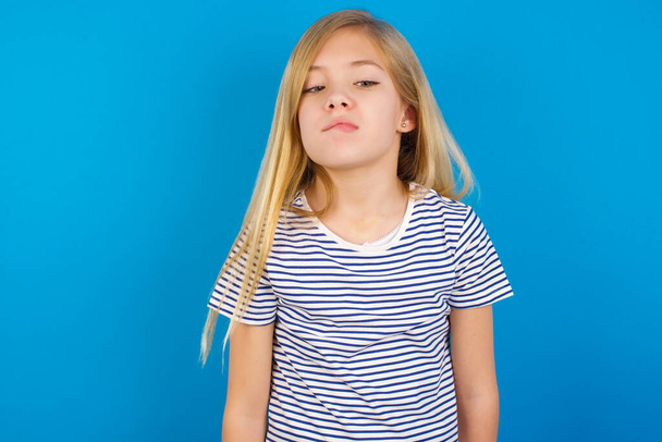 blank meisje draagt gestreept shirt tegen blauwe muur grimas en gek gezicht, schreeuwend uit de hand, grappig gek uit te drukken vrijheid en wild. - Foto, afbeelding