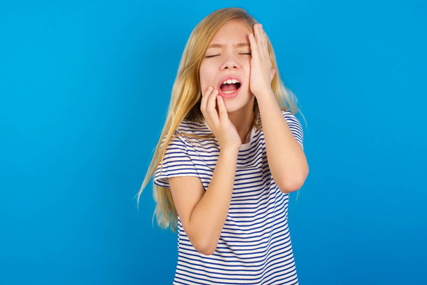Doleful zoufalý pláč běloška dívka nosí pruhované tričko na modré zdi, vypadá stresující, mračí tvář, cítí osamělý a úzkostlivý - Fotografie, Obrázek