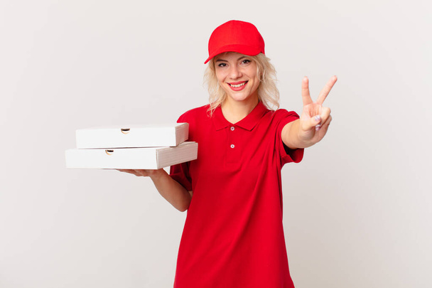 young pretty woman smiling and looking happy, gesturing victory or peace. pizza delivering concept - Photo, image