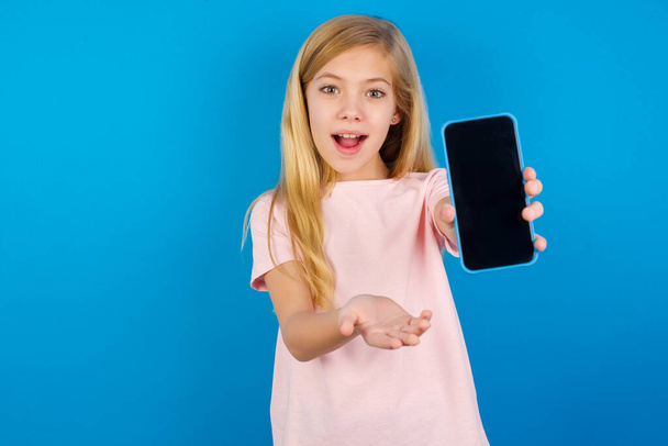 Valkoihoinen tyttö punaisessa paidassa sinistä seinää vasten kännykällä. esittää älypuhelin. Mainoskäsite. - Valokuva, kuva