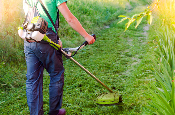 petrol cutter, grass trimmer close-up. Lawn care . worker cuts the grass with a trimmer on gasoline - Photo, Image