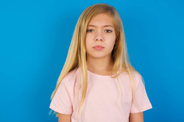 Biała dziewczynka w różowej koszuli na tle niebieskiej ściany przygnębiona i martwiąca się o niepokój, płacząca wściekła i przerażona. Smutne wyrażenie. - Zdjęcie, obraz