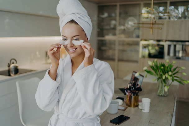 Szczęśliwa kobieta w szlafroku i ręcznik na głowie robi zabiegi kosmetyczne lub kosmetyczne w domu - Zdjęcie, obraz