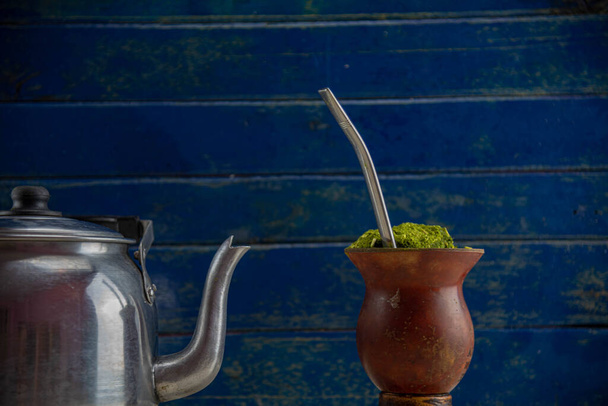 Pluimvee kalebas of kalebas met yerba mate ilex paraguariensis. Chimarro is een Zuid-Amerikaanse drank achtergelaten door inheemse culturen. Chimarro geïsoleerd in half licht op houten ondergrond. - Foto, afbeelding