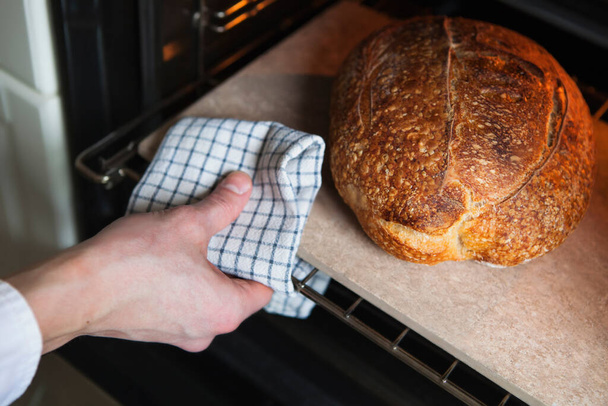 Человек достает из духовки домашний теплый хлеб - Фото, изображение