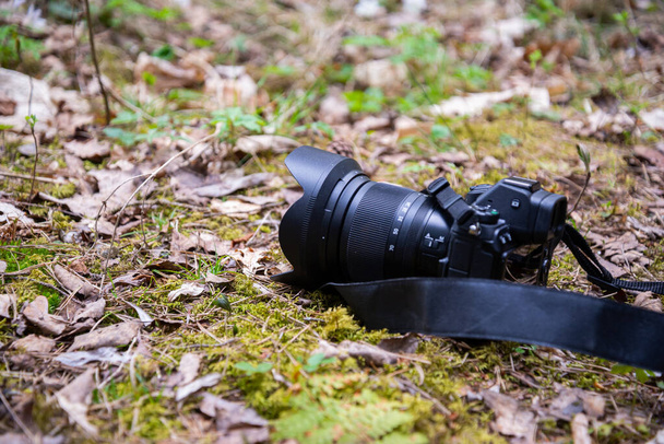 Primer plano de una cámara profesional en el bosque sobre musgos verdes y hojas de otoño. Fondo borroso. Macro fotografía - Foto, Imagen