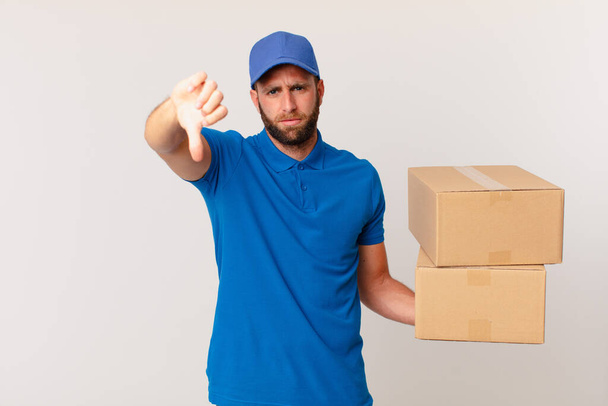 young handsome man feeling cross,showing thumbs down. package delivering concept - Foto, Imagen