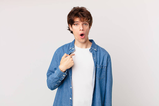 young handsome man looking shocked and surprised with mouth wide open, pointing to self - Foto, Bild
