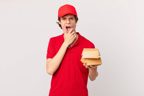 burger deliver man with mouth and eyes wide open and hand on chin - Foto, imagen