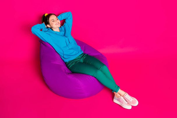 Full length photo of cute woman dressed blue hoodie rest purple bean bag closed eyes arms behind head isolated pink color background - Foto, afbeelding