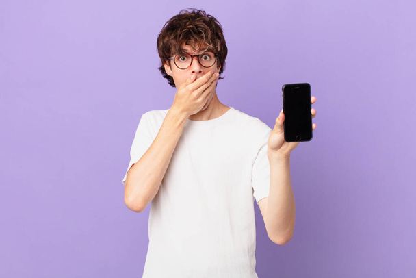 young man covering mouth with hands with a shocked and holding a cell - Foto, immagini