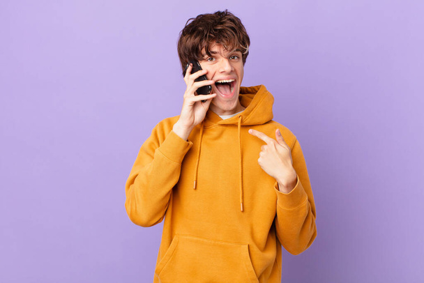 young man holding a cell feeling happy and pointing to self with an excited - Foto, immagini