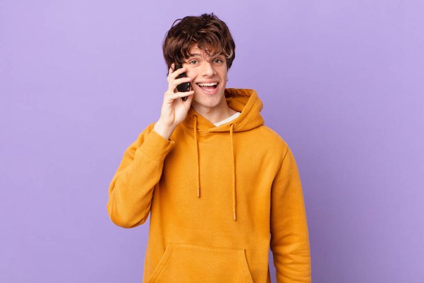 young man holding a cell looking happy and pleasantly surprised - Foto, immagini