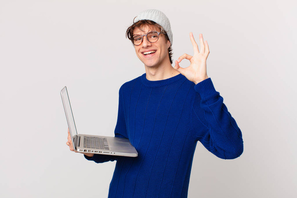 young man with a laptop feeling happy, showing approval with okay gesture - Photo, image