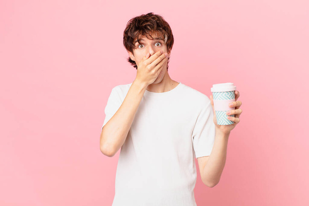 young man with a coffee covering mouth with hands with a shocked - Foto, imagen