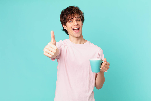 young man with a coffee mug feeling proud,smiling positively with thumbs up - Foto, afbeelding
