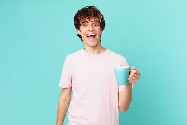 νεαρός άνδρας με μια κούπα καφέ φαίνεται χαρούμενος και ευχάριστα έκπληκτος - Φωτογραφία, εικόνα